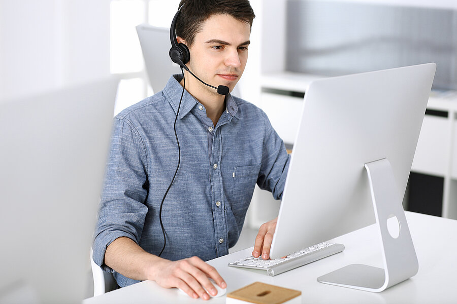 Arbeiter an iMac mit Headset in blauem Hemd