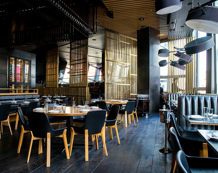 Hotelrestaurant mit dunklem Holzboden, schwarzen Stühlen und Holz-Elementen